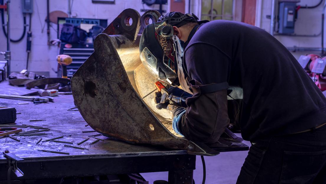 Person wearing welding gear working on a machine part