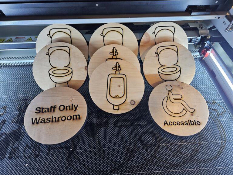 Laser-cut wooden restroom signs by Aesthetics by Lindsay Ann, featuring icons for toilets, urinals, staff-only washrooms, and accessible facilities, beautifully displayed on a work surface.