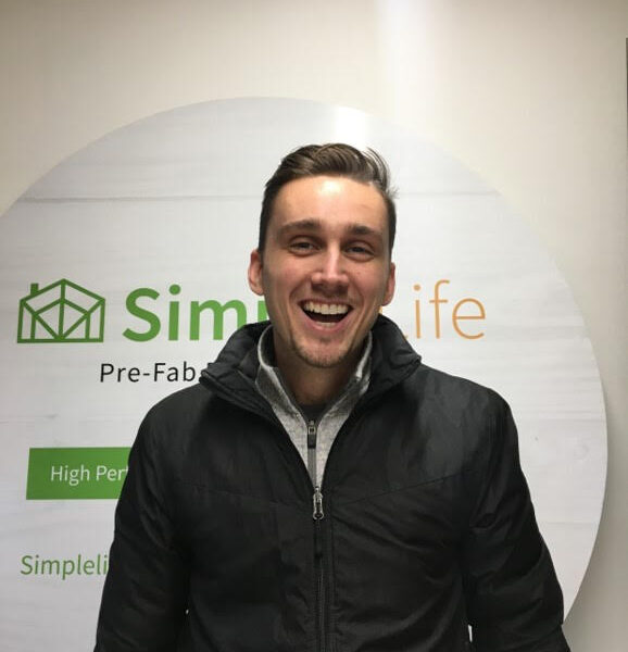 A man in a black jacket smiles in front of a round sign that reads "Simple Life Pre-Fab," proudly highlighting it as Canadian Made EH!.