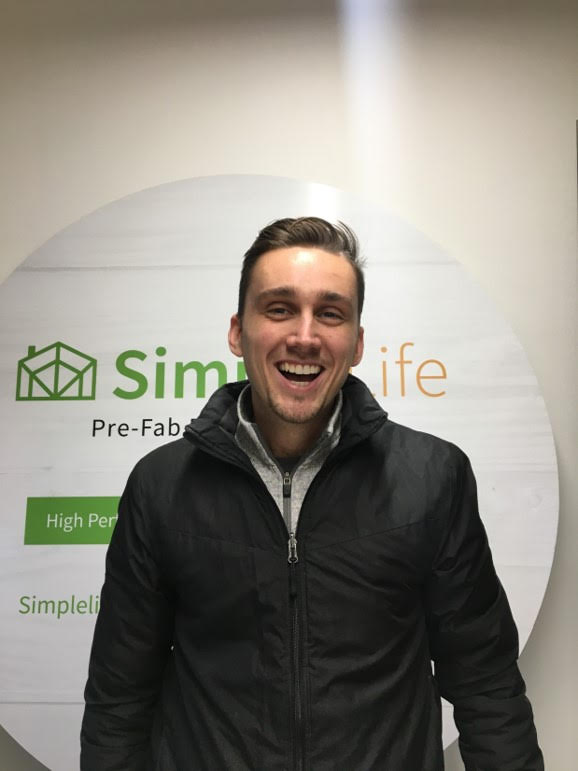 A man in a black jacket smiles in front of a round sign that reads "Simple Life Pre-Fab," proudly highlighting it as Canadian Made EH!.