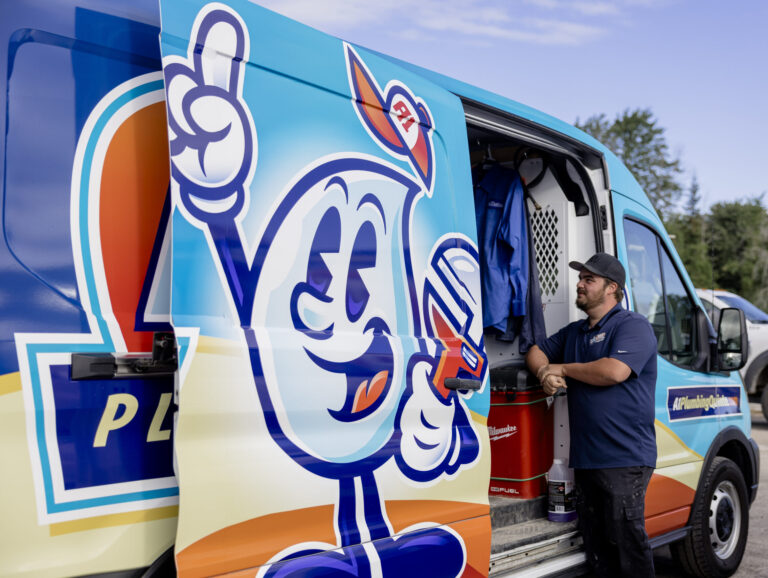 A man stands beside a colorful service van with a large cartoon mascot painted on the side, holding the vehicle's open sliding door—a proud moment for Bay of Quinte entrepreneurs.