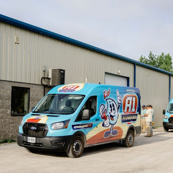 A blue A1 Plumbing van parked outside a beige industrial building, with two workers standing nearby, showcases professionals working in the trades.