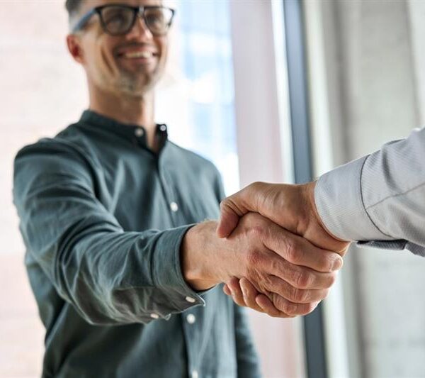 Two people shake hands indoors, highlighting marketing basics. One person's face is visible and smiling, while the other is out of frame except for their arm.