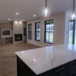 Modern open-concept living space with a marble kitchen island, dark cabinetry, pendant lights, and large windows—perfect for Bay of Quinte entrepreneurs seeking a cozy living area with a stone fireplace and stylish built-in shelving.